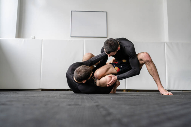 two men brazilian jiu jitsu bjj grappling drill technique or sparring at training at gym academy guard position martial arts copy space - Valokuva, kuva