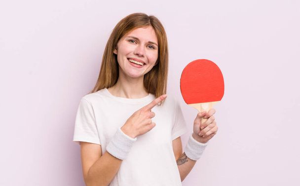 redhead pretty girl smiling cheerfully, feeling happy and pointing to the side. ping pong concept - 写真・画像