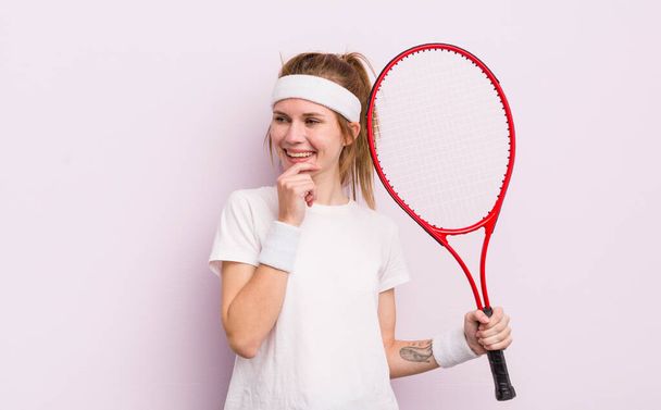 rothaarige hübsche Mädchen lächelt mit einem glücklichen, selbstbewussten Gesichtsausdruck mit der Hand am Kinn. Tenniskonzept - Foto, Bild
