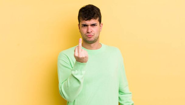 young handsome man feeling angry, annoyed, rebellious and aggressive, flipping the middle finger, fighting back - Photo, image