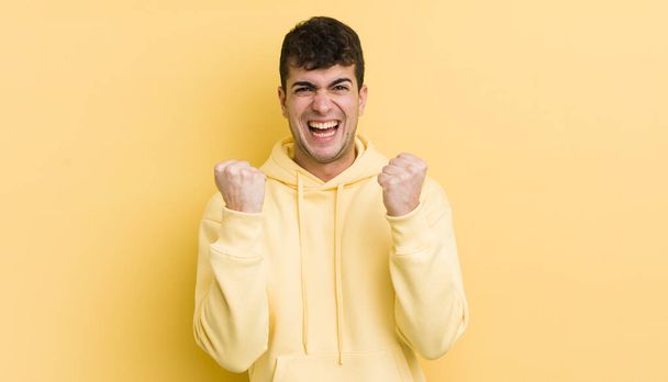 young handsome man shouting triumphantly, laughing and feeling happy and excited while celebrating success - Фото, изображение