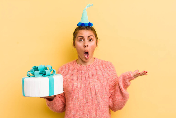 young pretty woman looking surprised and shocked, with jaw dropped holding an object. birthday concept - Foto, Bild