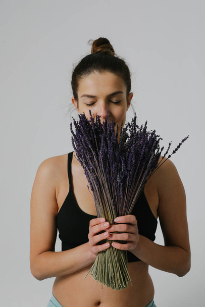 Vertical portrait of young caucasian woman with lavender, posing on white wall. - Фото, изображение