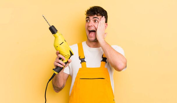 young handsome man feeling happy, excited and surprised. handyman and drill concept - Fotoğraf, Görsel