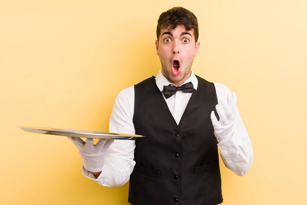 young handsome man amazed, shocked and astonished with an unbelievable surprise. waiter and tray concept - Foto, Imagem