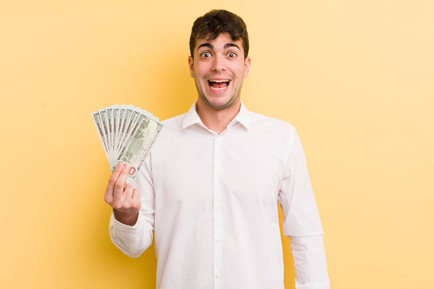 young handsome man looking happy and pleasantly surprised. money concept - 写真・画像