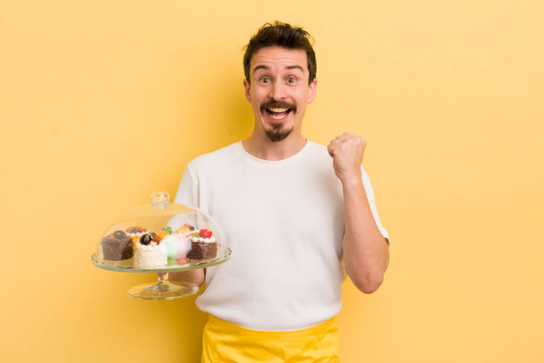 young handsome man feeling shocked,laughing and celebrating success. home made cakes concept - Fotoğraf, Görsel