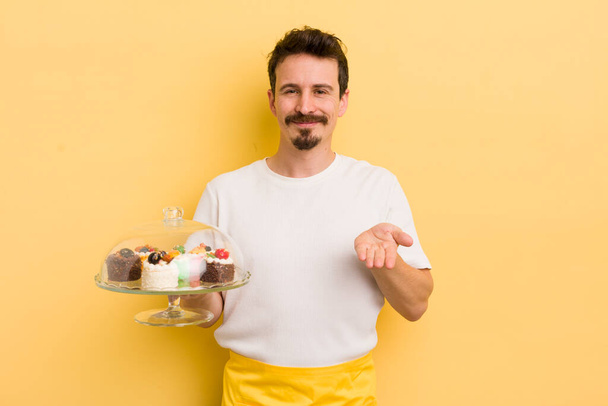 young handsome man smiling happily with friendly and  offering and showing a concept. home made cakes concept - Fotoğraf, Görsel