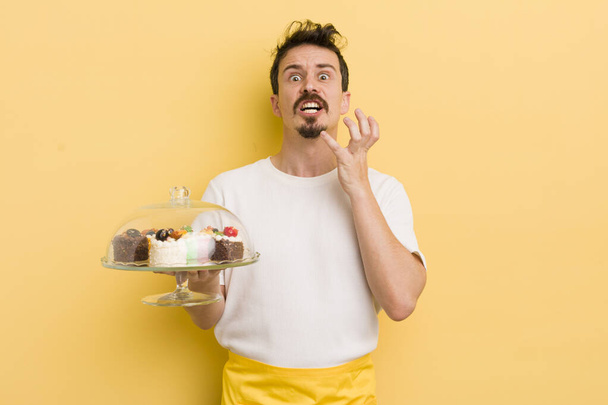 young handsome man looking desperate, frustrated and stressed. home made cakes concept - Fotoğraf, Görsel