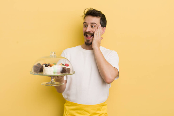 young handsome man feeling happy, excited and surprised. home made cakes concept - Foto, Imagem