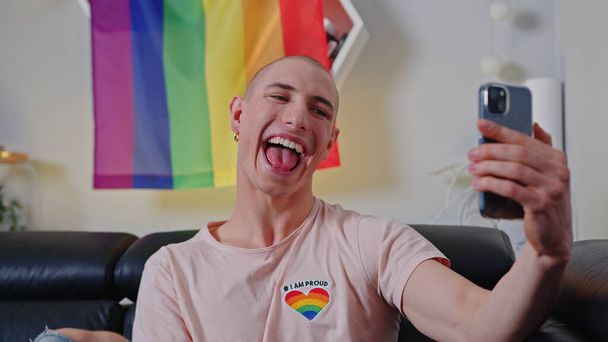 Divertido no binario europeo influencer persona toma un selfie delante de un arco iris orgullo bandera. - Foto, imagen