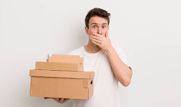 young handsome man covering mouth with hands with a shocked. shipping boxes concept - Fotoğraf, Görsel