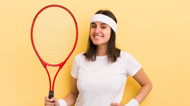 young hispanic woman smiling happily with a hand on hip and confident. tennis concept - Foto, Bild