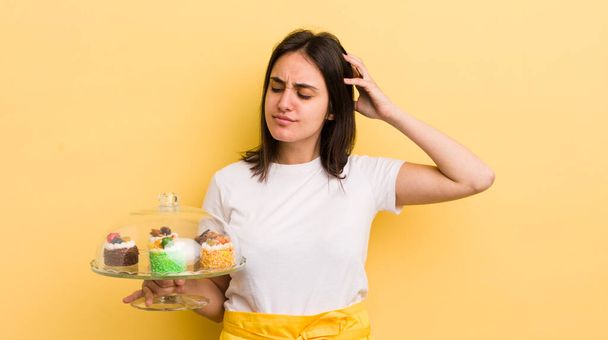 young hispanic woman smiling happily and daydreaming or doubting. home made cakes concept - Foto, Bild