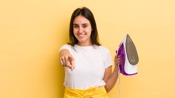 young hispanic woman pointing at camera choosing you. clothes iron concept - Foto, Imagen