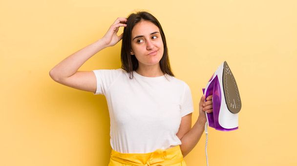 young hispanic woman smiling happily and daydreaming or doubting. clothes iron concept - Foto, Bild