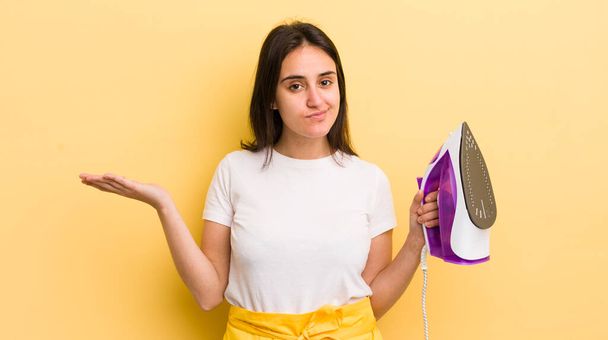 young hispanic woman feeling puzzled and confused and doubting. clothes iron concept - Photo, Image