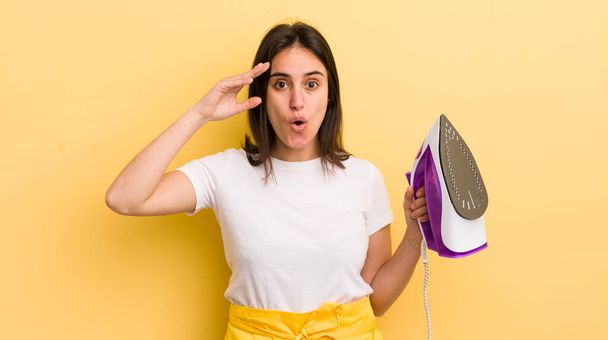 young hispanic woman looking happy, astonished and surprised. clothes iron concept - Фото, зображення
