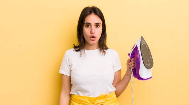 young hispanic woman looking very shocked or surprised. clothes iron concept - Foto, afbeelding