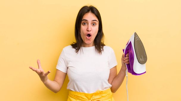 young hispanic woman amazed, shocked and astonished with an unbelievable surprise. clothes iron concept - Fotoğraf, Görsel