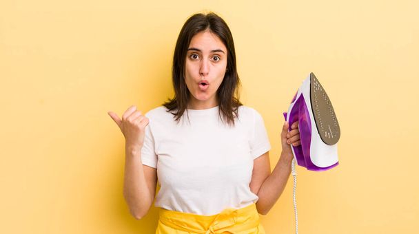 young hispanic woman looking astonished in disbelief. clothes iron concept - 写真・画像