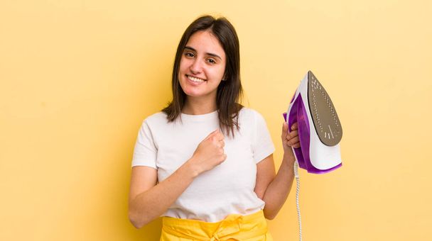 young hispanic woman feeling happy and facing a challenge or celebrating. clothes iron concept - Φωτογραφία, εικόνα