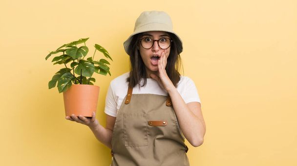 young hispanic woman feeling shocked and scared. gardener and plant concept - Foto, Imagen