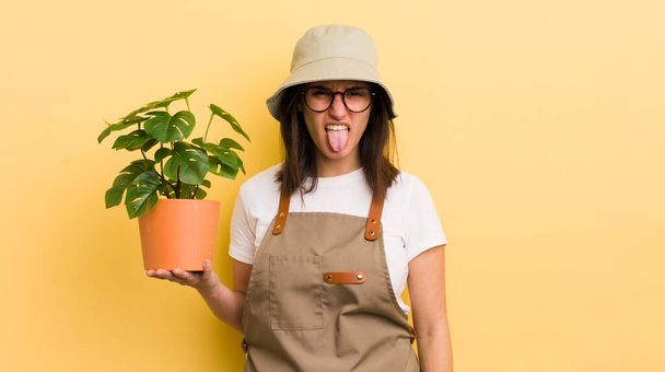 young hispanic woman feeling disgusted and irritated and tongue out. gardener and plant concept - Foto, Imagem