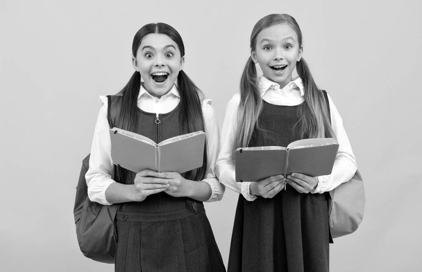 Verrast kinderen in formele uniformen lezen schoolboeken gele achtergrond, bibliotheek - Foto, afbeelding