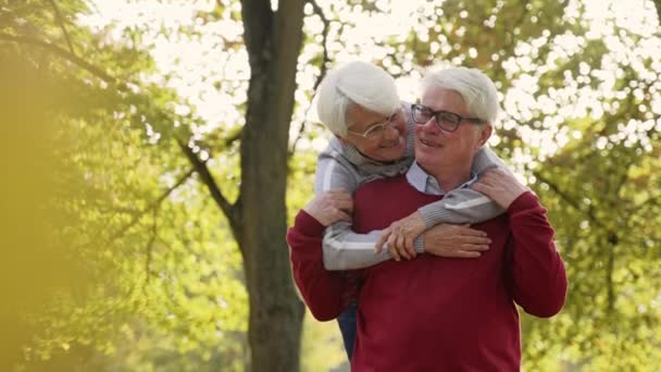 Happy elderly marriage has fun in the park. Elderly pensioner gray-haired lady hugging her beloved husband. - Footage, Video