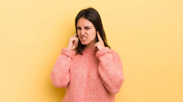 young hispanic woman looking angry, stressed and annoyed, covering both ears to a deafening noise, sound or loud music - 写真・画像