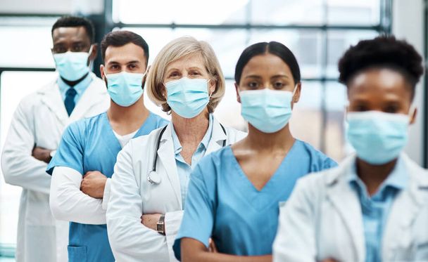 Trabajar en primera línea con los pacientes durante la pandemia. Retrato de un grupo de médicos que usan mascarillas mientras están de pie juntos en un hospital. - Foto, imagen