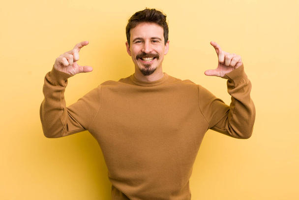 young hispanic man framing or outlining own smile with both hands, looking positive and happy, wellness concept - Φωτογραφία, εικόνα