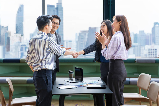 アジアのビジネスチームリーダーは、超高層ビルの見える現代的なオフィスの職場で握手をすることで、優れた業績チームパフォーマンスのためにチームメイトの従業員を祝福します - 写真・画像