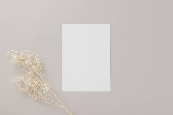 Puste zaproszenie kartka okolicznościowa Mockup 5x7 na brązowej kopercie z suszonymi kwiatami na beżowym tle, płaskie leżaki, makieta - Zdjęcie, obraz