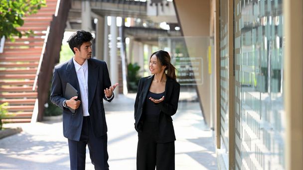 Guapo asiático hombre de negocios en traje formal caminando con asistente femenina a lo largo aparte fuera de su edificio de oficinas.  - Foto, Imagen