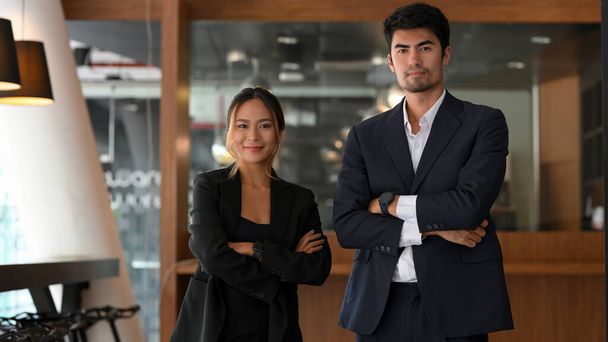 Kendine güvenen ve başarılı Asyalı genç iş adamları ve resmi takım elbiseli işadamları kollarını kavuşturup ofislerinde duruyorlar.. - Fotoğraf, Görsel