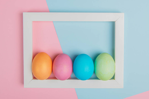 cuatro huevos en un marco blanco sobre un fondo rosa-azul - Foto, imagen
