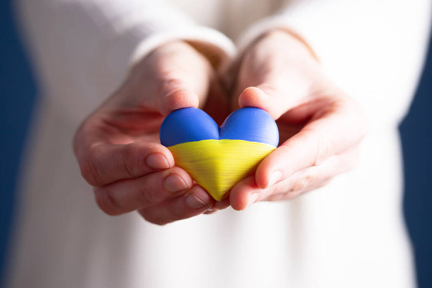 Heart shaped flag of Ukraine in female hands. The concept of solidarity with the citizens of Ukraine. - Photo, Image
