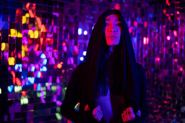 Close-up portrait of an androgenic model in a hood. Male transgender in studio with neon light. - Valokuva, kuva