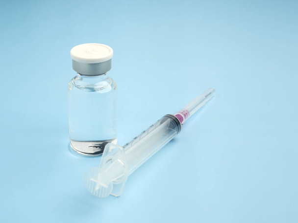 The vaccine in glass bottles with a syringe placed on a light blue background. Vaccine for immunization, and treatment from virus infection. Top view. Concept of medical and healthcar. - Photo, Image