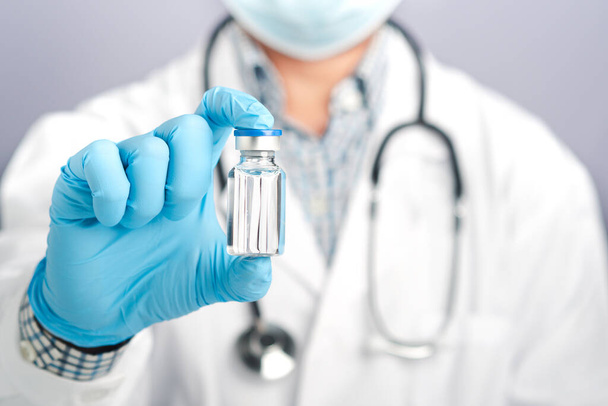 Doctor showing a vaccine bottle against a gray background. Vaccine for immunization, and treatment from virus infection. Close-up photo. Concept of medical and the fight against the virus. - Photo, Image