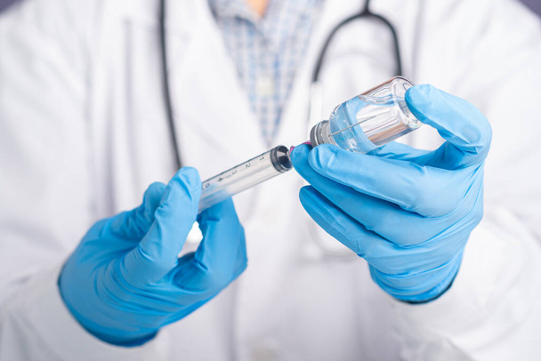O médico vestindo um uniforme branco, luvas médicas segurando uma seringa e um frasco de vacina para preparar a vacinação. Vacina para imunização e tratamento da infecção pelo coronavírus. - Foto, Imagem