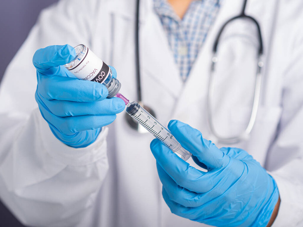 Γιατρός φορώντας λευκή στολή, ιατρικά γάντια κρατώντας μια σύριγγα, και COVID- 19 φιάλη εμβολίου για προετοιμάζει τον εμβολιασμό. Εμβόλιο για ανοσοποίηση και θεραπεία από λοίμωξη από τον κορωναϊό. - Φωτογραφία, εικόνα
