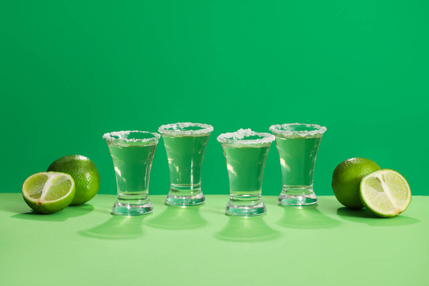 Shots of tasty tequila and limes on color background - Photo, Image