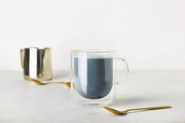 Glass cup of Charcoal Latte and spoon on light table - Photo, Image