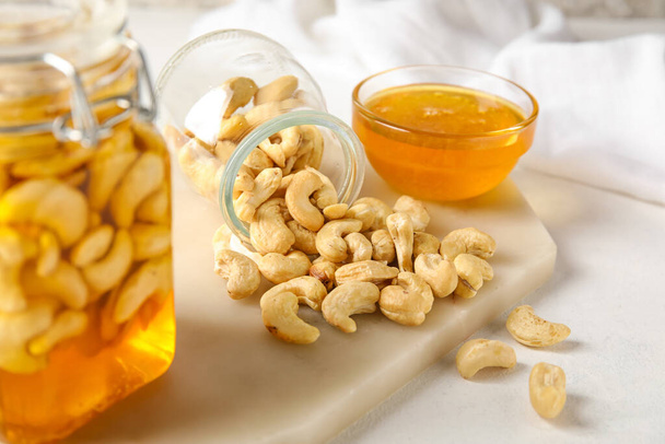 Βάζο με νόστιμα καρύδια κάσιους και γλυκό μέλι σε ελαφρύ φόντο - Φωτογραφία, εικόνα