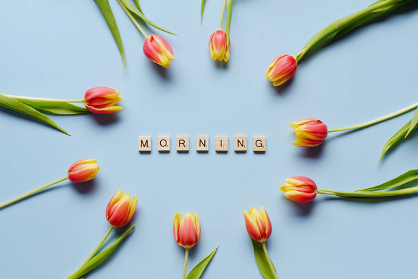 Yellow, red tulips on blue background. Word: morning. Alphabet cube beads. Top view, copy space. Flat lay. Spring holidays.  - Photo, Image