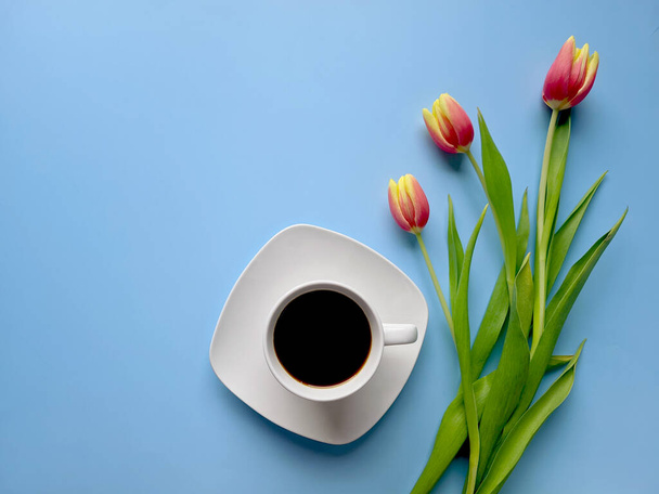Morning with cup of hot coffee and sweet donuts on blue background. Bouquet of tulips. Top view, copy space, mockup. Flat lay. Food and drinks. Spring holidays.  - Photo, Image
