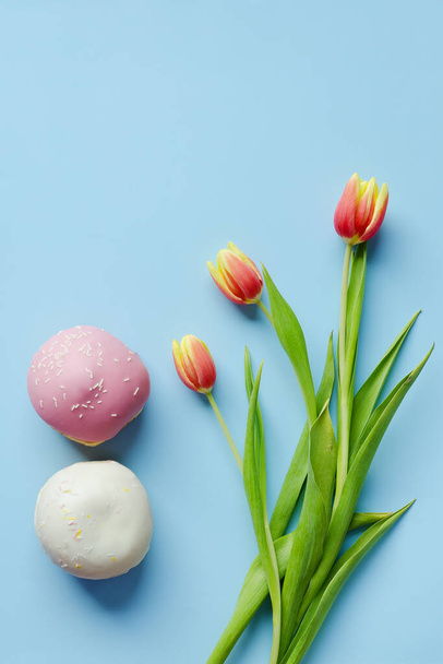 Morning with cup of hot coffee and sweet donuts on blue background. Bouquet of tulips. Top view, copy space, mockup. Flat lay. Food and drinks. Spring holidays.  - Foto, imagen